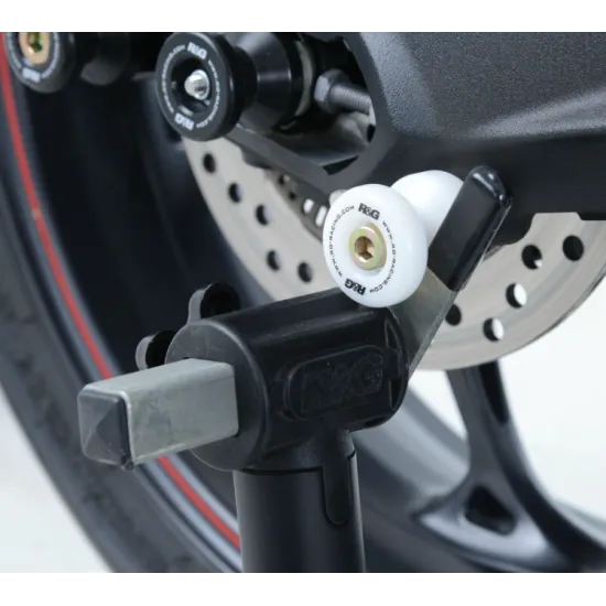 Черни адаптери R&G Racing Stand Bobbins с бяло лого, монтирани на задния шарнир на мотоциклет BMW/Triumph с офсетна пластина